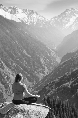 Black and white image, in which a young woman meditating on a mountain on the background of a very beautiful valley.の写真素材