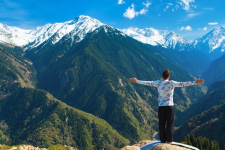 The young man is doing a yoga asana Sun Salution on the summit. On the background is a range of high tops of mountains.の写真素材