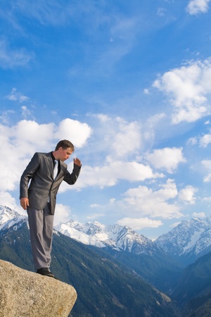 Image of a businessman standing on the top of the mountain, looking down. In the background a beautiful panorama of the valley with high peaks.の写真素材