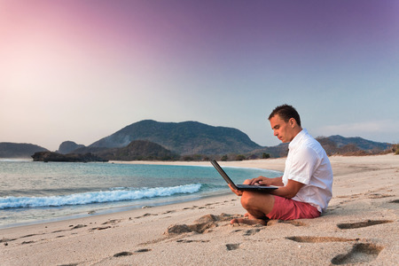 man uses laptop remotely at the beachの写真素材