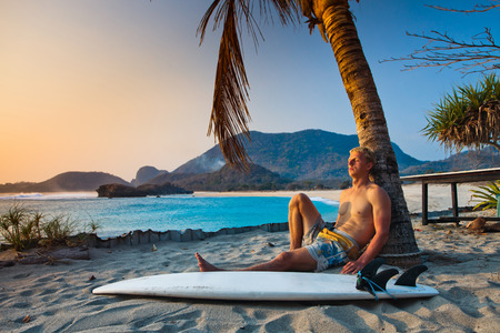 Surfer near the palm with surfboard on beachの写真素材