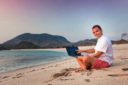 man uses laptop remotely at the beachの写真素材