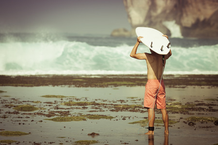 Man surfer with surfboard on a coastline. Bali, Indonesiaの写真素材