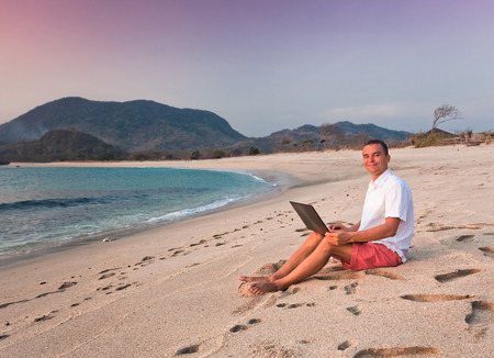 man uses laptop remotely at the beachの写真素材