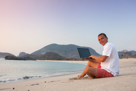 man uses laptop remotely at the beachの写真素材
