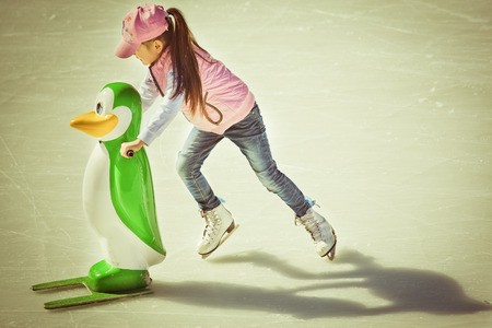 Adorable little girl in winter clothes and hat skating on ice rink at Canadaの写真素材