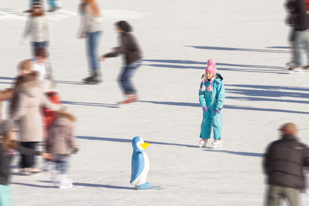 Adorable little girl in winter clothes and hat skating on ice rink at Canadaの写真素材