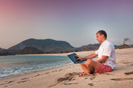 man uses laptop remotely at the beachの写真素材