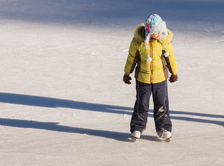 Adorable little girl in winter clothes and hat skating on ice rink at Canadaの写真素材