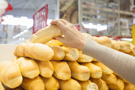 woman packs a French baguette in a plastic bag at supermarketの写真素材
