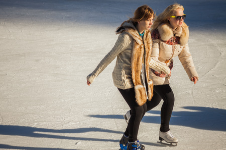 two girls of teenagers ice skating and holding hands at the Medeoの写真素材