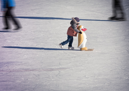 Adorable little boy in winter clothes and hat skating on ice rink at Canada
