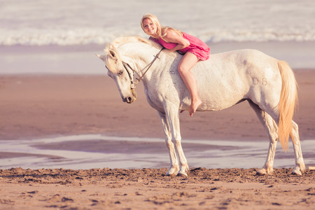 Beautiful young woman lies and hugs a horse, she is happy to engage in a hobbyの写真素材