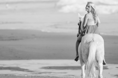 Black and white image of Beautiful young woman riding a horse along the beachの写真素材