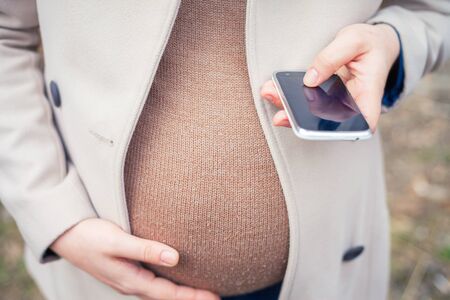 pregnant woman outdoor, calling to ambulance by mobile phoneの写真素材