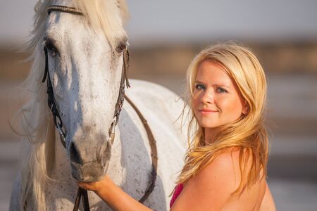 Beautiful young woman near a horse, she is happy to engage in a hobbyの写真素材