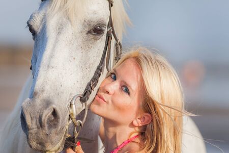 Beautiful young woman near a horse, she is happy to engage in a hobbyの写真素材