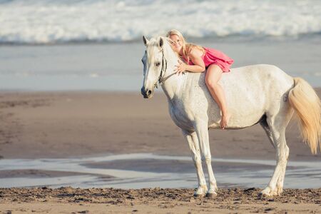 Beautiful young woman lies and hugs a horse, she is happy to engage in a hobbyの写真素材