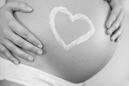 Pregnant woman with concept of love, heart applied as a stretch mark cream, black and white editionの写真素材
