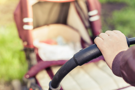 foreground of baby carriage and mothers hand at outdoor, spring or summer season with fresh green backgroundの写真素材