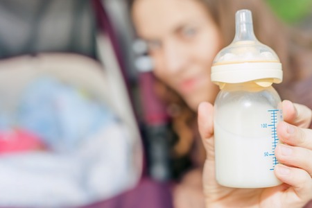background of happy mom holding at hand baby bottle with milk at foregroundの写真素材
