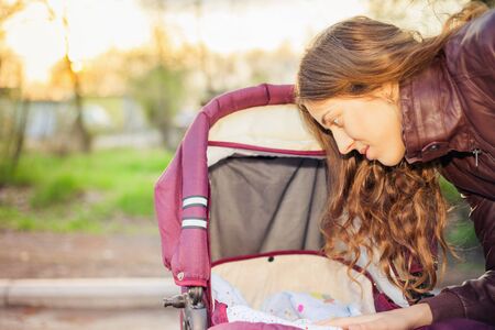 happy mother at outdoor wearing a spring jacket shakes a baby carriage