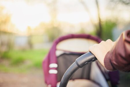 foreground of baby carriage and mothers hand at outdoor, spring or summer season with fresh green backgroundの写真素材