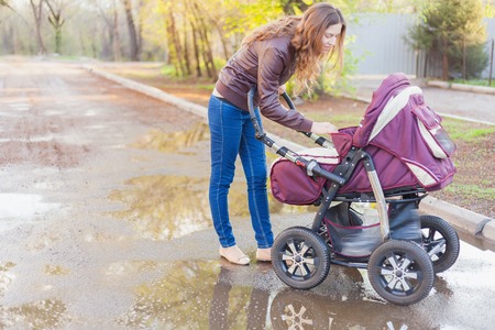 mother at outdoor shakes a baby carriage at spring or autumn season with large copy space for any...