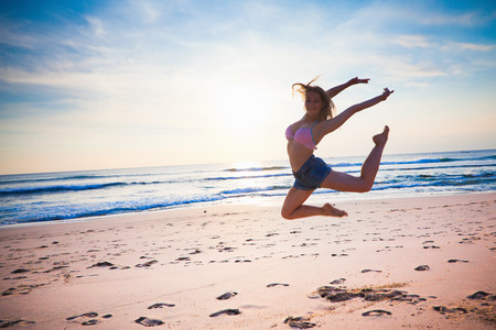 young girl dancing at the beach at blue sky background, summer vacation with joyの写真素材
