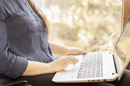 Beautiful happy student with a laptop sitting against a bright window. Young woman learn and using a...