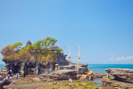 Horizontal image on the background of the foaming waves with rocky shore. In the foreground many tourists walking near the Pura Uluwatu. Bali, Indonesia.の写真素材