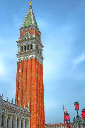 Picture the top of the tower on the main square of Venice against the backdrop of bright blue sky. In the foreground a beautiful old streetlight. Italy.の写真素材