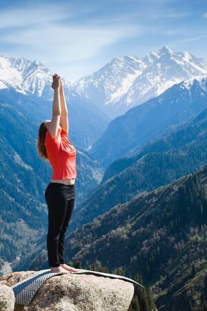 The young woman is doing a yoga asana âSun Salutionâ on the summit. On the background is a range of high tops of mountains.の写真素材