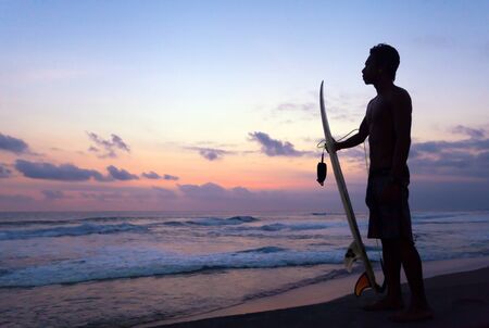 Indonesian surfer standing at sunset in Ocean in Bali, Indonesia