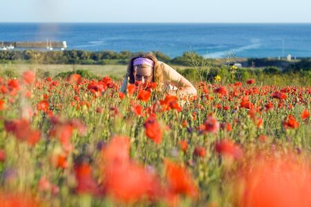 Image of a young girl in bright red flowers - poppies at sunset. In the background is visible sea horizon the coast of Finisterre, Plogoff, France.の写真素材