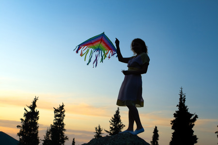 A young silhouette women flying kite at a sunset summer day.の写真素材