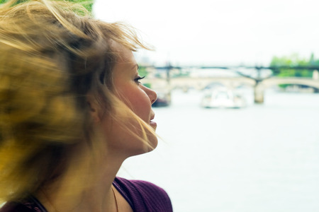 Image of a young girl, whose hair is dissipated in the wind. In the background is seen the bridge over the Seine River and sailing tour-ship.の写真素材