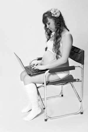 Black and white portrait of pregnant woman on a white background in the studio, where the mom uses the computer to search for information about the child.の写真素材