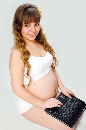 Portrait of pregnant woman on a white background in the studio, where the mom likes the computer to search for information about the child.の写真素材