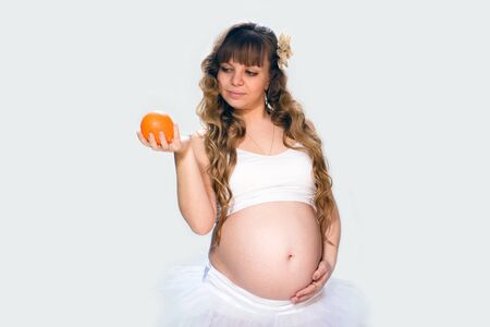 Portrait of pregnant woman with a orange on a white background in the studio.の写真素材