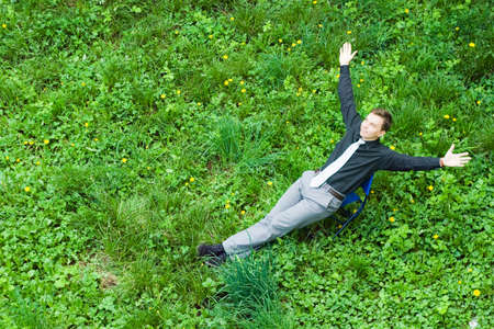 Image of a contented businessman sitting on the grass in the nature. The sign of success raised a...