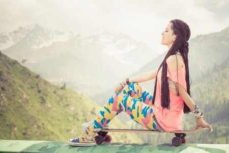 Hippie young and beautiful girl with skateboard outdoor at mountain. Longboard is the most popular...