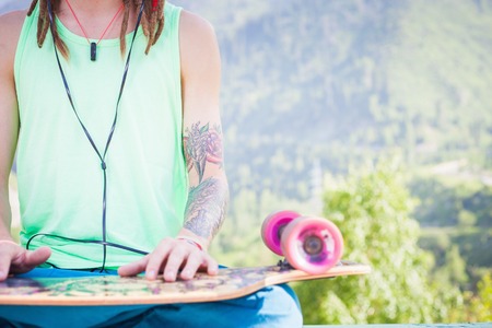 Closeup Hipster relaxing and handsome man listening to music with skateboard outdoor at mountain. ?oncept of meditation on a background of natureの写真素材