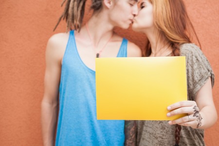 Fashion teenagers couple kissing and holding yellow frame at red background.の写真素材
