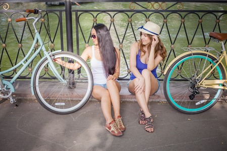 Beautiful young women dressed in short shorts resting after travel by city vintage bicycle at summer...