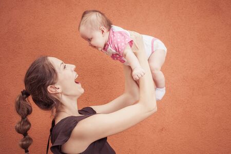 Happy young mother throw up baby on a background of orange wall.