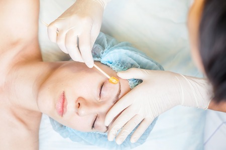 Beautiful woman in spa salon receiving epilation or correction eyebrow using sugar - sugaring. You...