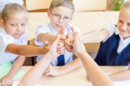 Successful group of children or kids at school classroom sitting at a desk and show a thumbs up gesture. Concept of achievement teamwork among studentsの写真素材