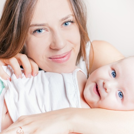 Happy baby girl lying near her mother on a white bed. Newborn with mom smiling and looking at...