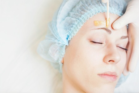 Closeup beautiful woman in spa salon receiving epilation or correction eyebrow using sugar - sugaring. You can see her smooth eyebrow after hair removalの写真素材